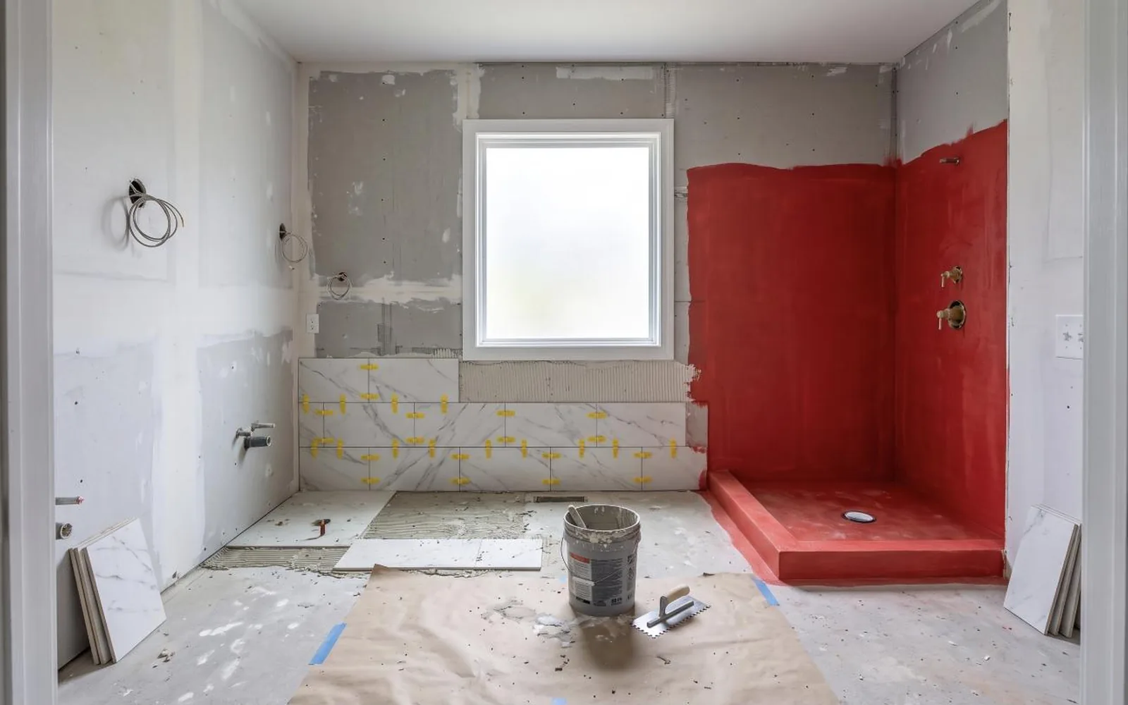 Shower walls sealed with red waterproofing membrane while porcelain tile is installed